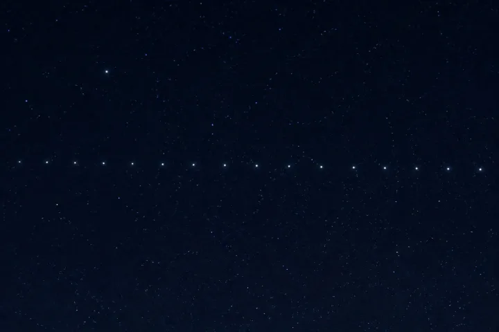 Una fila di satelliti Starlink visibile nel cielo notturno come puntini luminosi in movimento, fotografico realistico